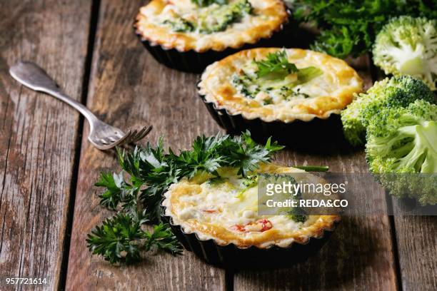 Baked homemade quiche pie in mini metal forms served with fresh greens and fork on old plank wooden background. Close up with space.
