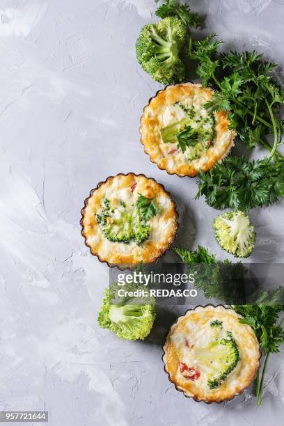 Baked homemade vegetable broccoli quiche pie in mini metal forms served with fresh greens on gray concrete background. Flat lay with copy space....