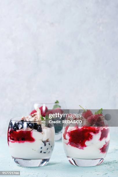 Traditional summer dessert Eton Mess. Broken meringue with whipped cream, berry jam, fresh blueberries and raspberries in two glasses, decorated with...