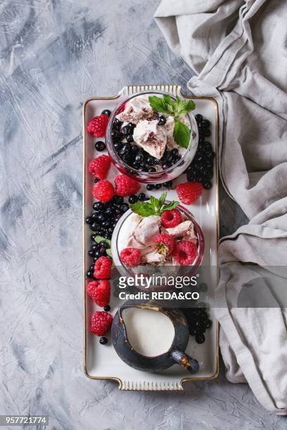 Traditional summer dessert Eton Mess. Broken meringue with whipped cream, berry jam, fresh blueberries and raspberries in two glasses, decorated by...