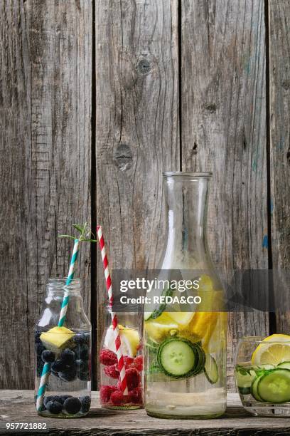 Citrus cucumber berries blueberry and raspberry sassy sassi water for detox in glass bottles with cocktail tubes on wooden background. Clean eating,...