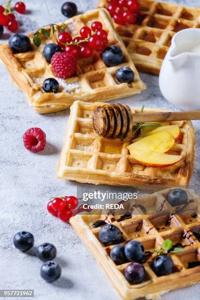 Homemade square belgian waffles with fresh ripe berries blueberry, raspberry, red currant, peach served with caramel, balsamic sauce, honey, jug of...