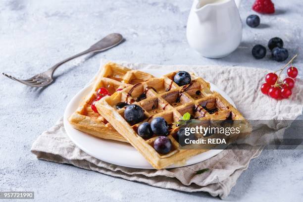 Breakfast with homemade square belgian waffles with fresh ripe berries blueberry, raspberry, red currant, balsamic sauce on white plate with jug of...
