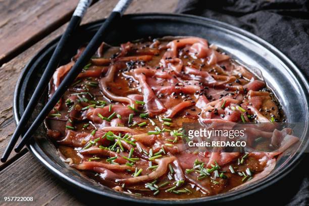 Asian style Beef carpaccio with soy sauce, chive onion, black sesame, served on vintage metal tray with textile napkin and chopsticks over old wooden...