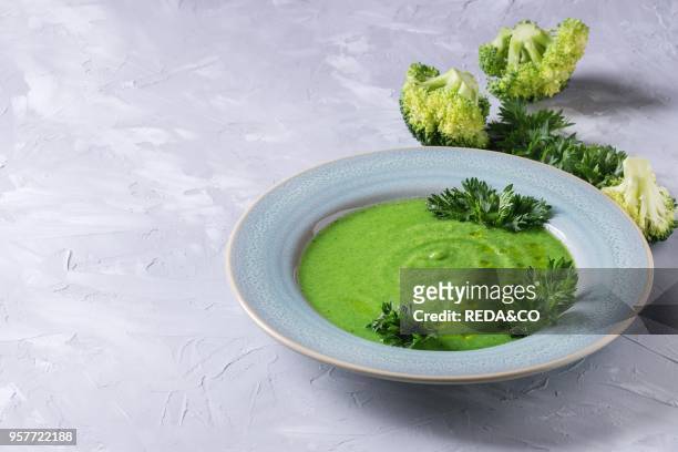 Vegetarian vegan broccoli cream soup served in blue plate with fresh parsley and broccoli over gray concrete background. Copy space. Healthy eating.