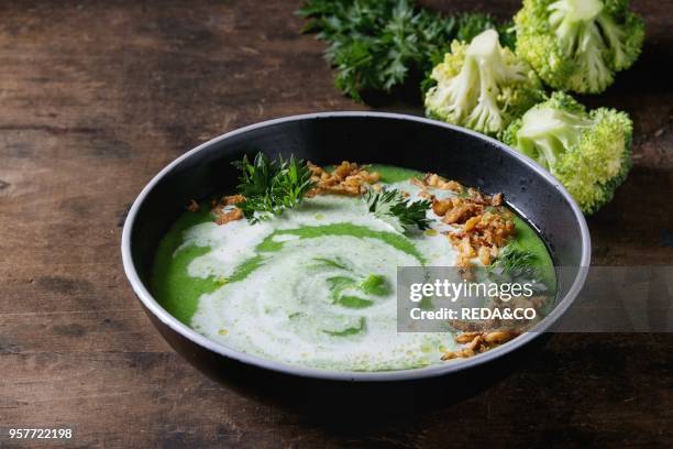 Vegetarian broccoli cream soup served in black bowl with cream, fried onion, fresh parsley and broccoli over old wooden background. Close up. Healthy...