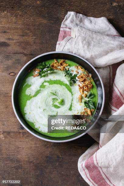 Vegetarian broccoli cream soup served in black bowl with cream, fried onion, fresh parsley, kitchen linen towel over old wooden background. Top view...