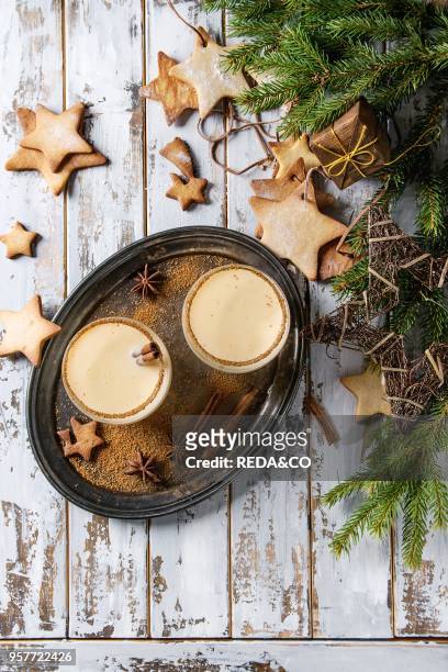 Eggnog Christmas milk cocktail with cinnamon, served in two glasses with shortbread star shape sugar cookies different size, decor toys, fir branch...