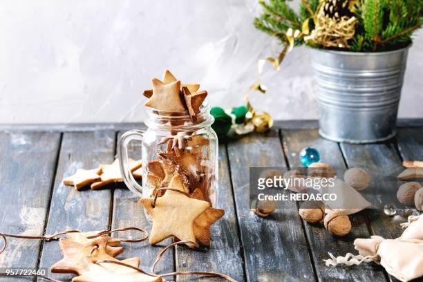 Homemade shortbread star shape sugar cookies different size in glass jar and as garland on old wooden table decorated by Christmas tree and gifts....