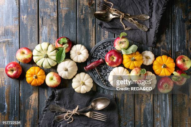 Autumn holiday table decoration setting with decorative pumpkins, apples, red leaves with vintage cutlery, red wine, candle over wooden table. Rustic...