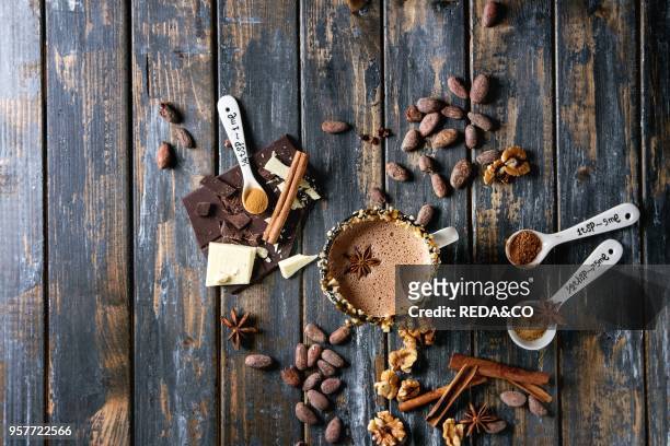 Vintage mug of hot chocolate, decor with nuts, caramel, spices. Ingredients above. Chopped dark and white chocolate, cocoa beans, anise over old...