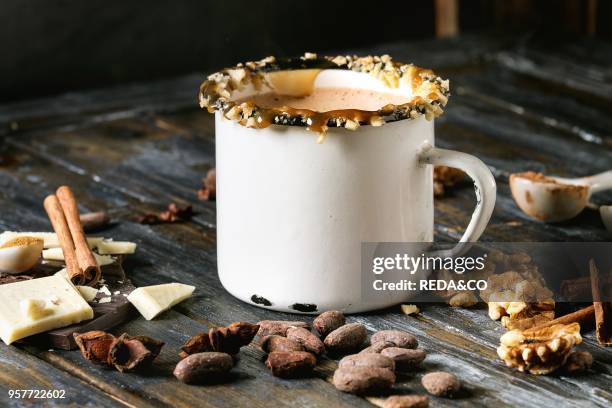 Vintage mug of hot chocolate, decor with nuts, caramel, spices. Ingredients above. Chopped dark and white chocolate, cocoa beans, anise over old...