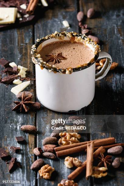 Vintage mug of hot chocolate, decor with nuts, caramel, spices. Ingredients above. Chopped dark and white chocolate, cocoa beans, anise over old...