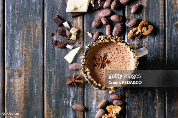 Vintage mug of hot chocolate, decor with nuts, caramel, spices. Ingredients above. Chopped dark and white chocolate, cocoa beans, anise over old...