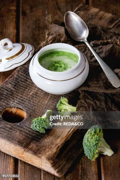 Vintage ceramic bowl with broccoli mashed and aioli sauce, served with spoon and sackcloth rag on wood chopping board over old wooden background....