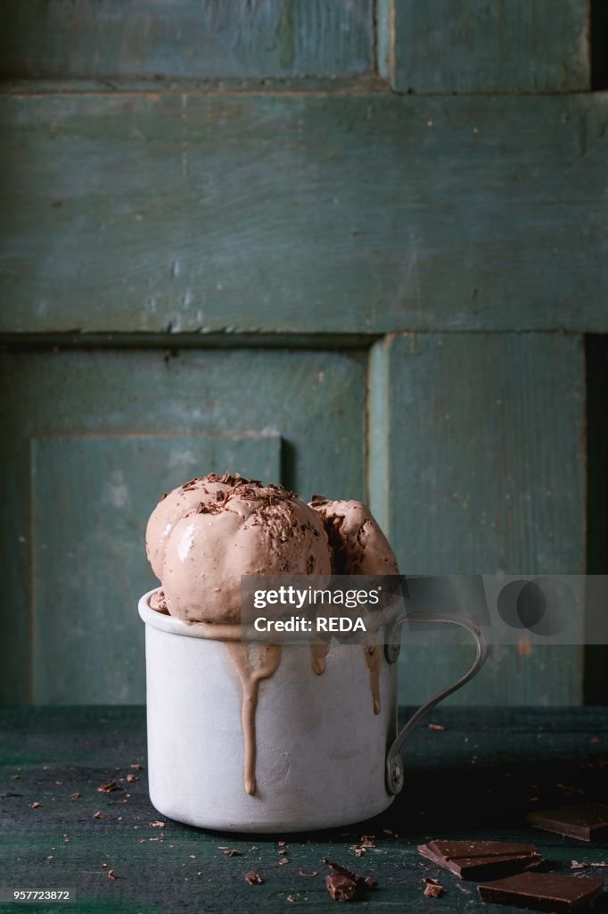 Frozen vintage aluminum mug with melting chocolate ice cream balls, served with chopped dark chocolate on old wooden table. Dark rustic style. Space for text