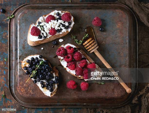 Set of dessert sandwiches with fresh berries blueberry and raspberry, cream cheese, thyme and honey, served with honey dipper over old dark iron...