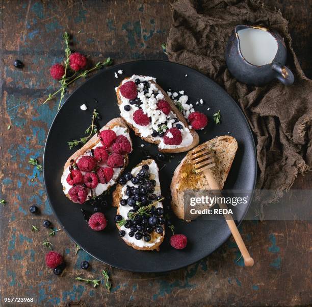 Set of dessert sandwiches with fresh berries blueberry and raspberry, cream cheese, thyme and honey, served with jug of milk on black plate over old...