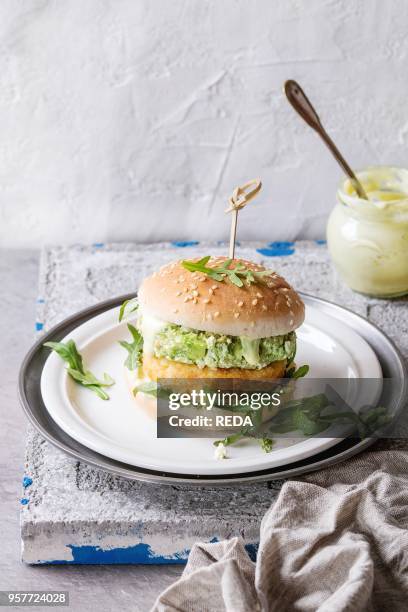 Vegetarian hamburger with onion and cheese cutlets, avocado salad, arugula and yogurt sauce in white plate over gray stone texture background....