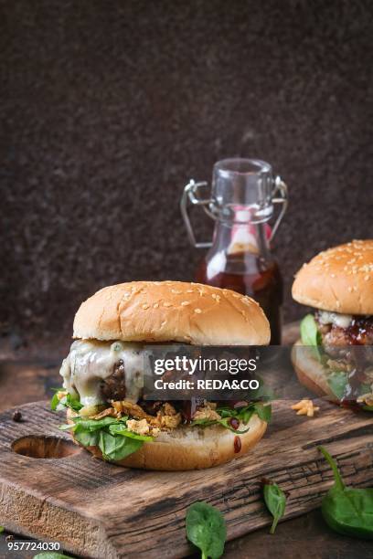 Two hamburgers with beef burger cutlet, fried onion, spinach, ketchup sauce and blue cheese in traditional buns, served on wood chopping board over...