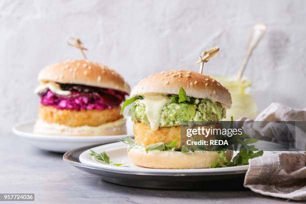 Two vegetarian hamburgers with onion and cheese cutlets, avocado salad, arugula, fried beetroot and yogurt sauce in white plate over gray texture...
