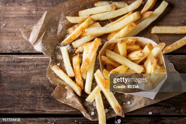 Fast food french fries potatoes with skin served with salt and herbs in lunch box on baking paper over old dark wooden background. Top view, space...
