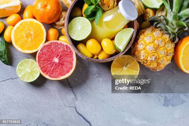 Variety of whole and sliced citrus fruits pineapple, grapefruit, lemon, lime, kumquat, clementine and physalis with mint and bottle of juice in bowl...