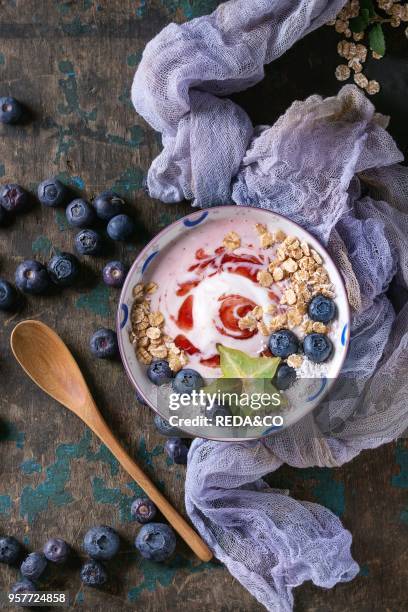 Smoothie bowl healthy breakfast. Strawberry yogurt with blueberries, granola, mint, jug of milk and carambola on textile gauze over dark wooden...