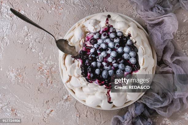 Homemade meringue cake Pavlova with whipped cream, sugar powder, fresh blueberries, blueberry sauce on vintage cake stand, shovel on beige concrete...