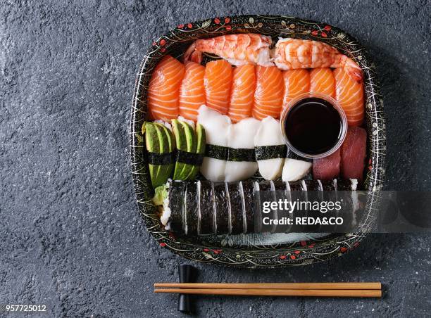 Sushi Set nigiri and sushi rolls on wooden serving board with soy sauce and chopsticks over black stone texture background. Top view with space....