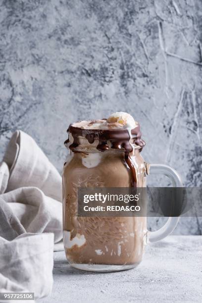 Chocolate coffee milkshake with ice cream scoop served in glass mason jar on gray texture background. Summer sweet drink.