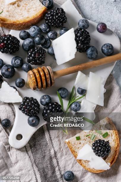 Berries blackberry and blueberry, honey on dipper, rosemary, sliced goat cheese with bread served on ceramic board with textile linen over gray...