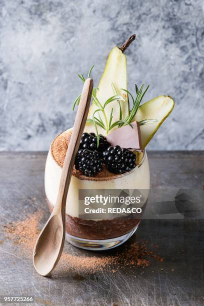 Dessert breakfast layered chia seeds, chocolate pudding, rice porridge in glass decorated by fresh blackberries, sliced pear, cocoa powder. Stand...