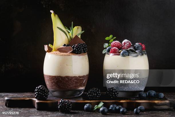 Various dessert breakfast layered chia seeds, chocolate pudding, rice porridge in glass decorated by fresh blackberries, sliced pear, cocoa powder....