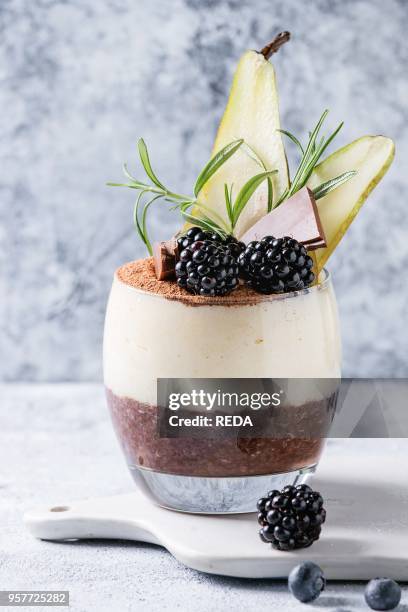 Dessert breakfast layered chia seeds, chocolate pudding, rice porridge in glass decorated by fresh blackberries, sliced pear, cocoa powder. Stand on...