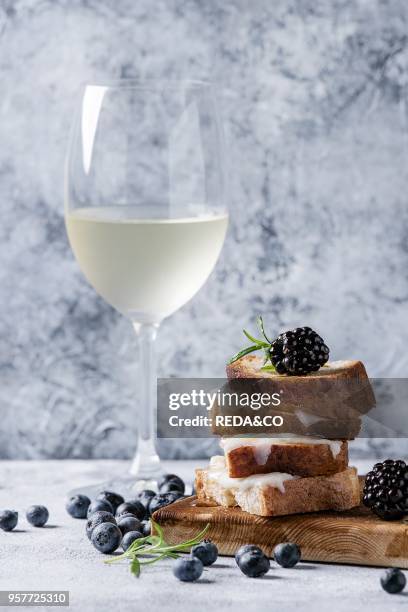 Grilled sandwich with melted goat cheese, blackberry, blueberry, rosemary and honey, served on wooden serving board with glass of cold white wine...