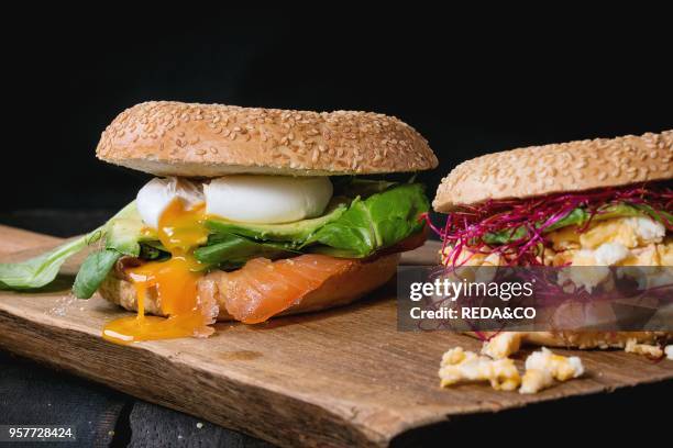 Two Bagels with salted salmon, spinach, beetroot sprouts, avocado scrambled and soft boiled egg with liquid yolk on wooden chopping board over old...