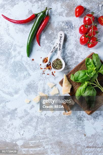 Ingredients for pasta sauce tomatoes, basil, chili peppers and parmasan cheese on wooden cutting board over white textured background. Flat lay.