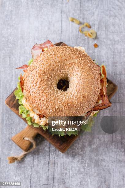 Bagel with stew beef, fresh salad and fried onion on small wooden chopping board over wooden background. Top view.