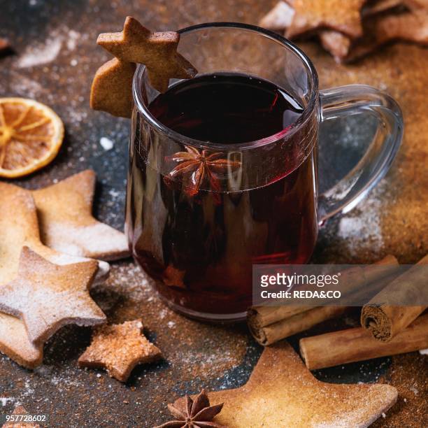 Glass mug of hot red mulled wine spices, sugar shortbread cookies star shape and cookie on glass, anise and cinnamon powder over dark textured...