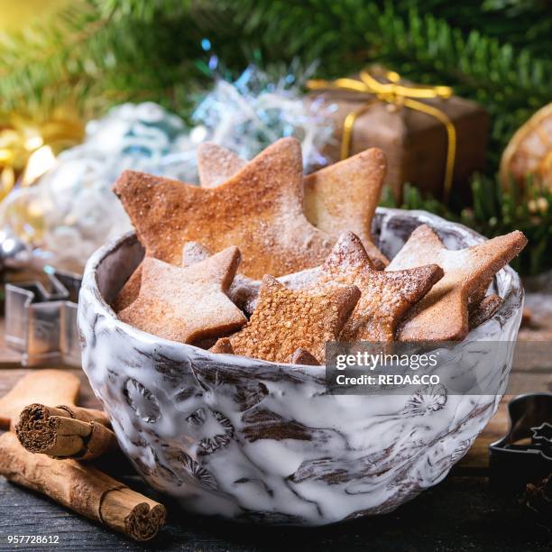 Bowl of homemade Christmas shortbread star shape sugar cookies different size with sugar powder and cookie cutters on old wooden surface with...