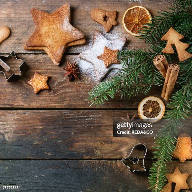 Homemade Christmas shortbread star shape sugar cookies different size with sugar powder, cinnamon, green fir tree and cookie cutters on wooden...