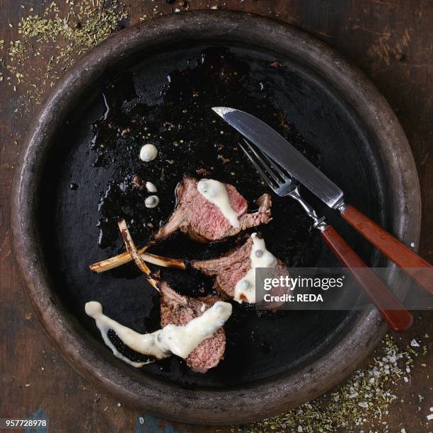 Chopped grilled bbq rack of lamb under pepper sauce,, served with seasoning, fork and knife on clay tray over old wooden background. Top view. Square...
