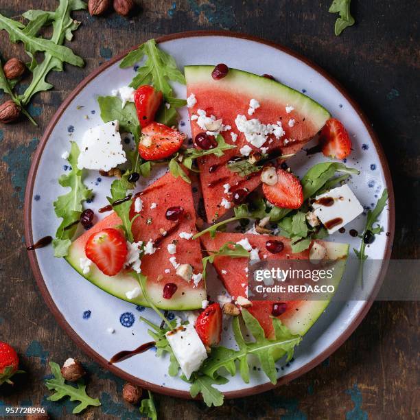 Blue spotted plate with watermelon and strawberry fruit salad with feta cheese, arugula, nuts and balsamic sauce, served over old dark wood...