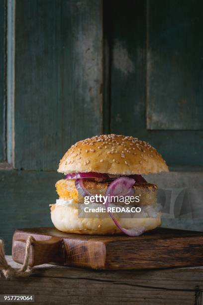 Homemade veggie burger with sweet potato, cottage cheese and red onion, served on wooden chopping board over old wooden background. Rustic style.