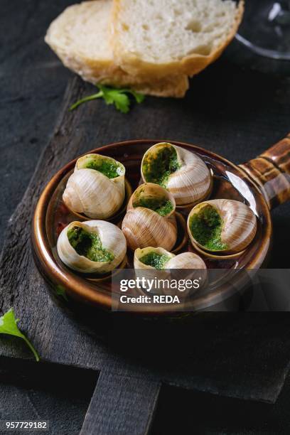 Escargots de Bourgogne - Snails with herbs butter, gourmet dish, in traditional ceramic pan with parsley and bread on wooden chopping board over...