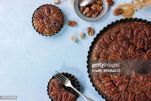 Homemade Big round caramel pecan pie and small tartlets in black iron forms, served with brown sugar, caramel sauce and vintage cutlery over blue...