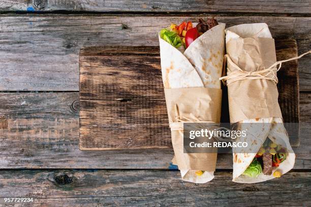 Mexican style dinner. Two papered tortillas burrito with beef and vegetables over old wooden background. Flat lay. With copy space.