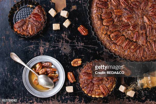 Homemade Big round caramel pecan pie and small tartlets in black iron forms, served with brown sugar, caramel sauce and vintage cutlery over old...