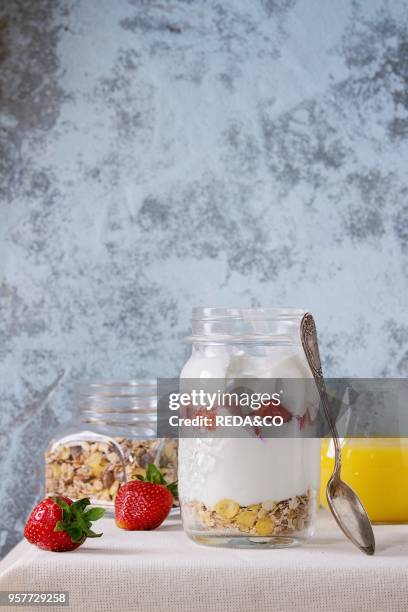 Healthy breakfast muesli, strawberries and yogurt with mango smoothie in glass mason jars. Served with fresh strawberry on white tablecloth with...